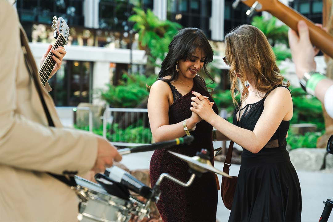 Two students dancing, they're wearing dark dresses and you can see a band playing around them