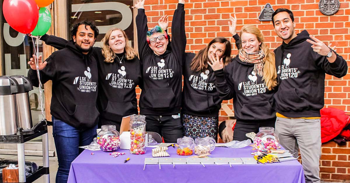 Students and Sabbatical Officers posing for a photo by the 100 Years of LSESU stall