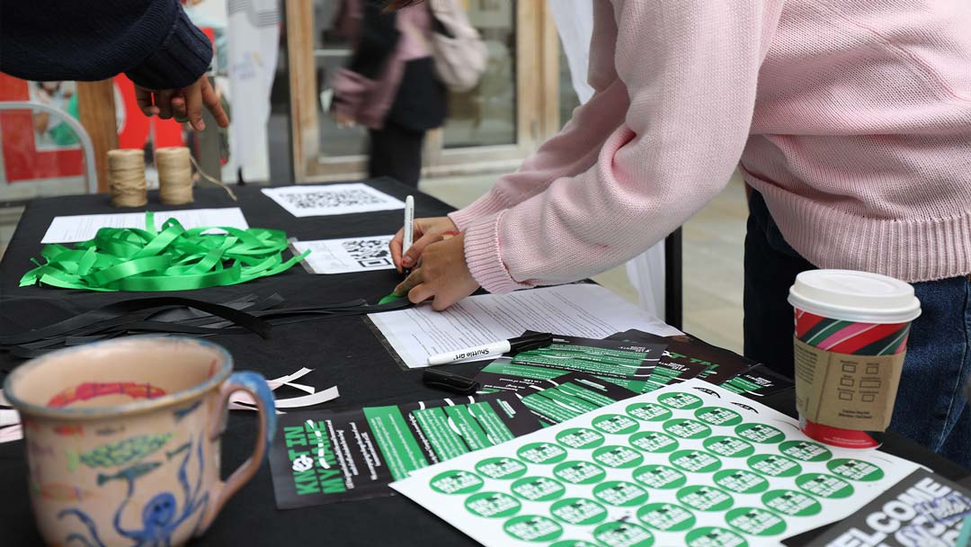A student leaning on a table writing their name on a knot as part of the Knot In My Name campaign