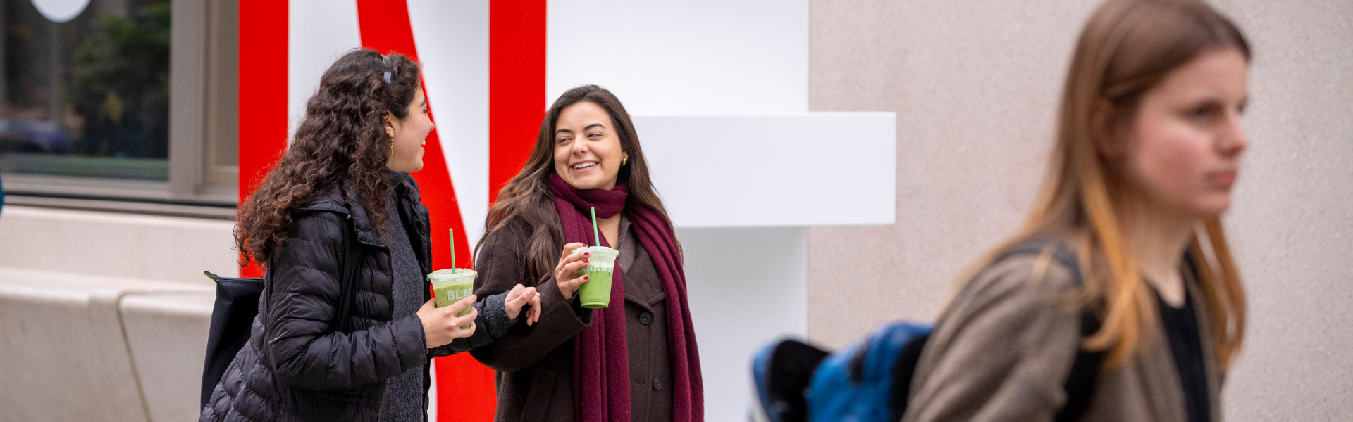 Two students drinking matcha in front of the LSE sign